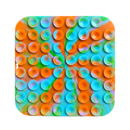 View of the back of a colorful square dog lick mat with circular patterns on a white background